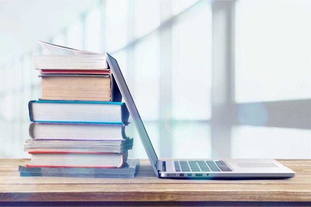 Laptop und Buecher auf Schreibtisch als Symbol fuer Organisation und Bachelorarbeiten schreiben lassen